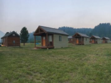 A photograph of modern cabins. Each has a covered porch and a front window.